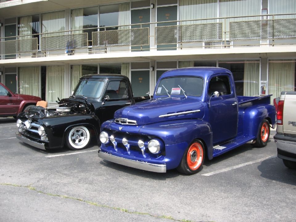 Blue 1951 Ford F-1 pickup truck with orange wheels parked next to a black pickup