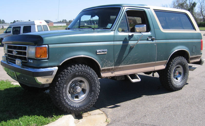 Green Ford Bronco with tan trim and aftermarket wheels parked on a sunny day