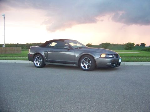 1993 Ford Bronco - A gray Ford Mustang convertible is parked on the side of a road during a cloudy sunset.