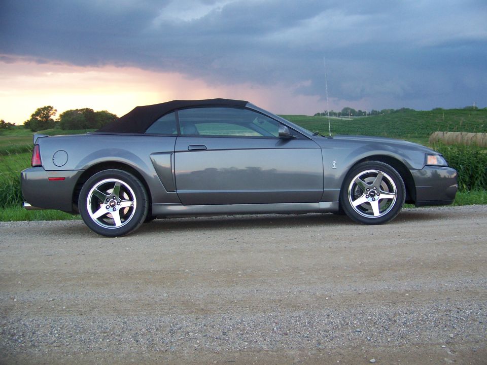 Gray Ford Mustang convertible parked on a dirt road with a cloudy sky
