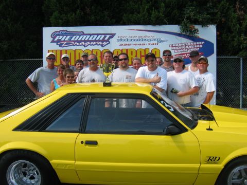 1992 Ford Mustang - A group celebrates with a trophy next to a yellow 1992 Ford Mustang GT at Piedmont Dragway.