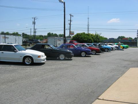1992 Ford Mustang - A row of cars are parked in a lot on a sunny day, with a service center visible in the background.