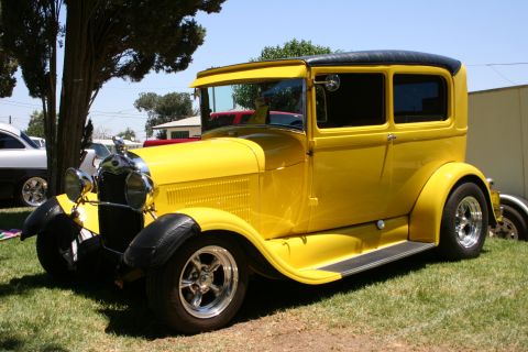1984 Ford Bronco - A vintage yellow sedan with a black roof and fenders sits on grass under a tree.