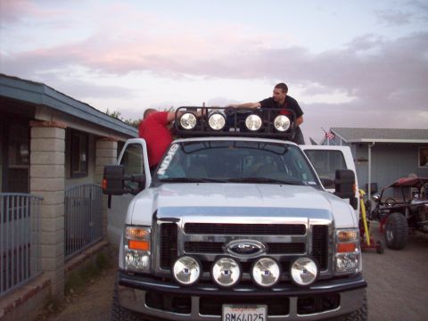 1995 Ford Bronco - White Ford Super Duty truck with auxiliary lights and two people working on the roof rack.