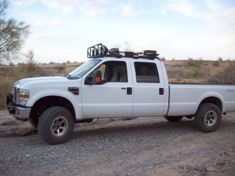 1995 Ford Bronco - This white pickup truck is equipped with a roof rack loaded with shovels and other tools.