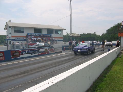 1992 Ford Mustang - Two cars compete on a drag strip with spectators in the stands.