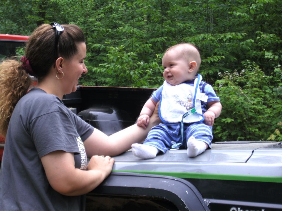 Baby in bib sitting on tailgate of pickup truck with woman