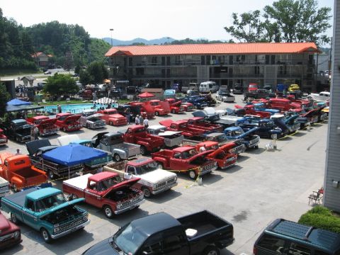 1966 Ford F-100 - A gathering of classic Ford F-Series trucks is displayed in a parking lot next to a motel with a swimming pool.