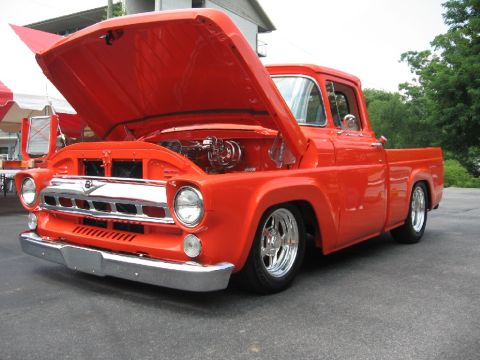 1966 Ford F-100 - A bright orange pickup truck is parked outside with its hood raised, revealing the engine bay.