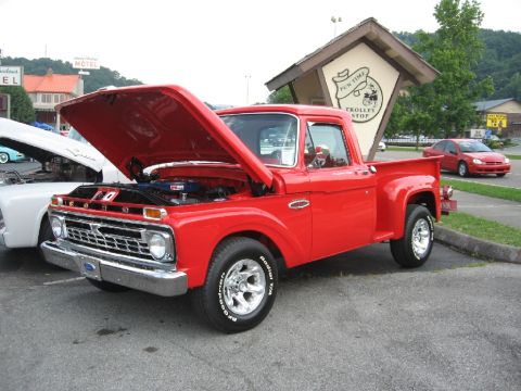 1966 Ford F-100 - A bright red 1966 Ford F-100 pickup truck is displayed with its hood open, revealing the engine compartment.
