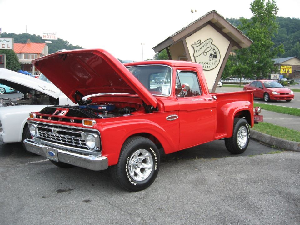 Red 1966 Ford F-100 pickup truck, hood open, showing engine. Chrome grille and wheels