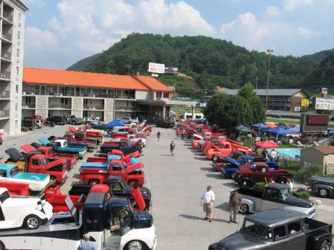 1966 Ford F-100 - A large gathering of pickup trucks are parked in a lot at a motel, with a mountain range visible behind the buildings.