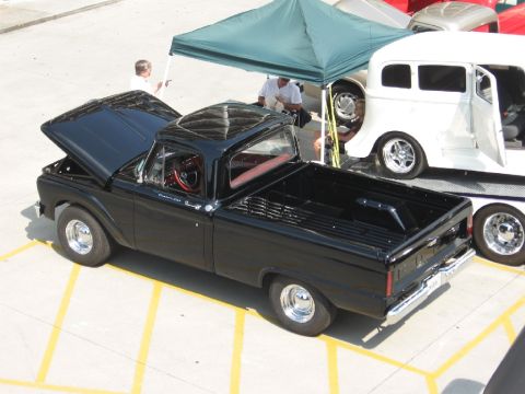 1966 Ford F-100 - A black pickup truck is parked next to a white van on a trailer under a green canopy.