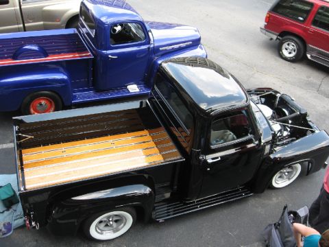 1966 Ford F-100 - A black 1953 Ford F-series truck with a polished wooden bed is parked next to a blue truck.