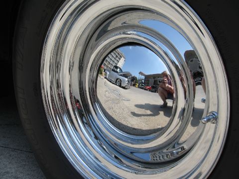 1966 Ford F-100 - Reflection in a chrome wheel shows a silver pickup truck and other vehicles at an outdoor event.