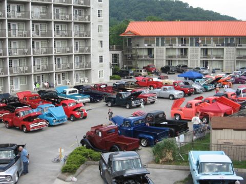 1966 Ford F-100 - A variety of pickup trucks are gathered in a parking lot in front of a hotel.