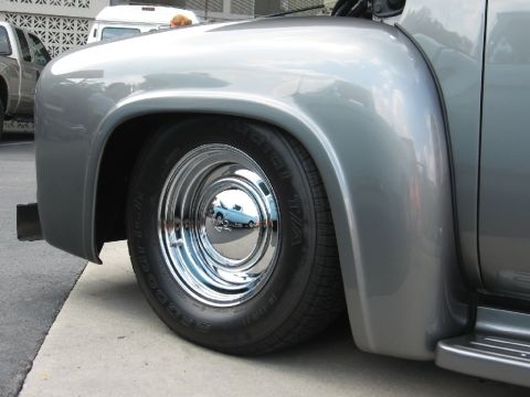 1966 Ford F-100 - A lowered 1950s Ford F-Series truck sits low on its suspension, with a reflection of another vehicle in its shiny hubcap.