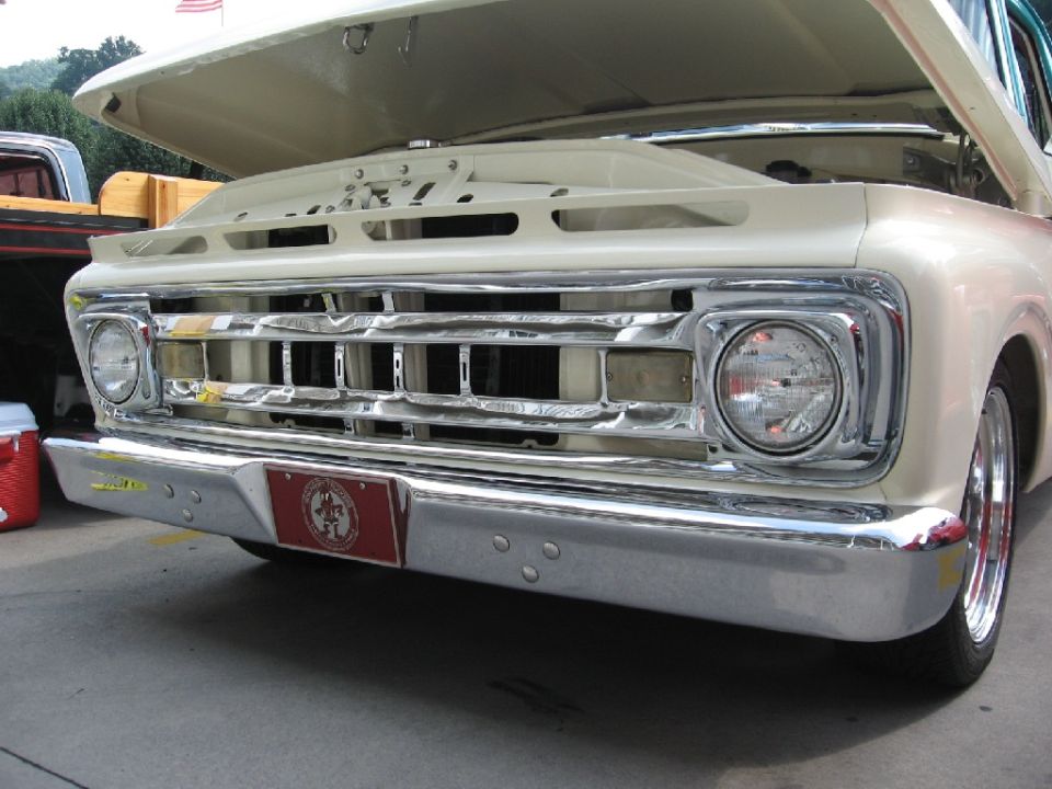 Cream-colored 1965 Ford F-100 truck front grille with chrome bumper and a red emblem