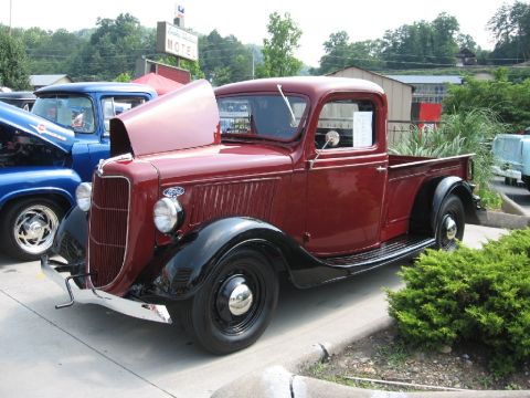 1966 Ford F-100 - A maroon 1935 Ford truck is parked with its hood open, alongside a blue truck, with a motel sign in the background.