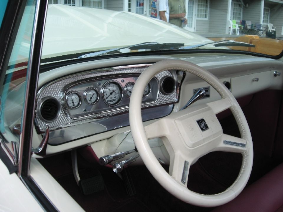 Dashboard and steering wheel of a classic car, with multiple gauges and a cream-colored wheel