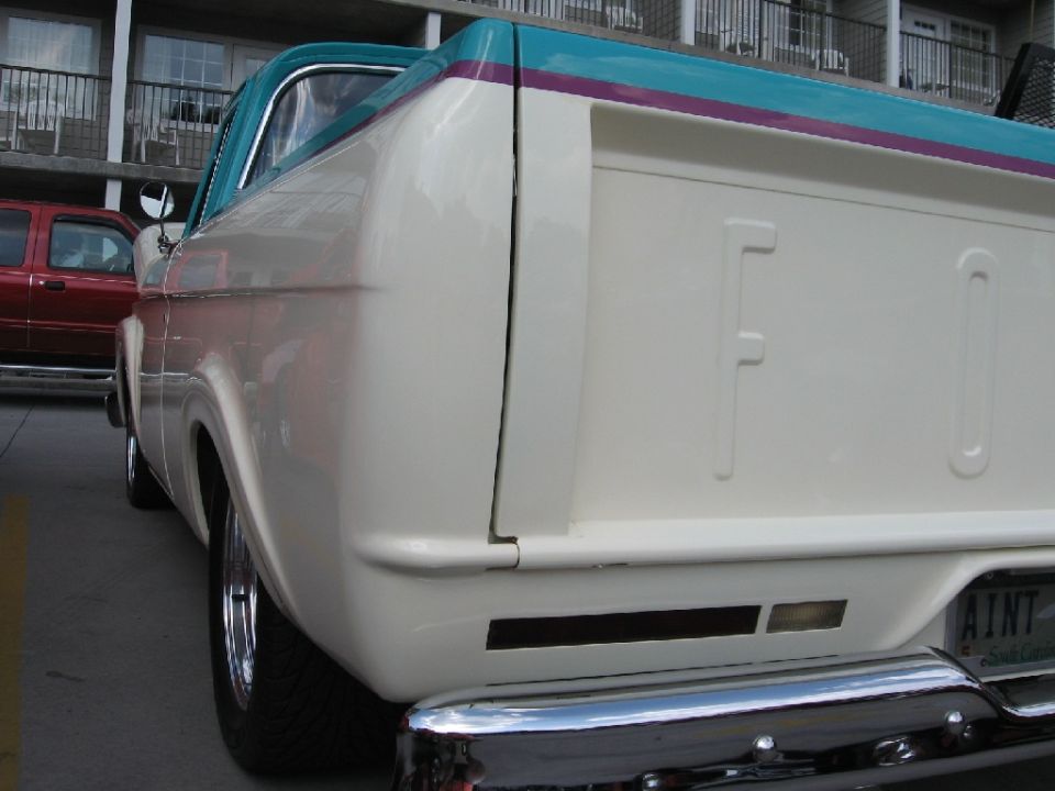 White 1965 Ford F-100 pickup truck, rear quarter view, teal and purple stripe on cab roof