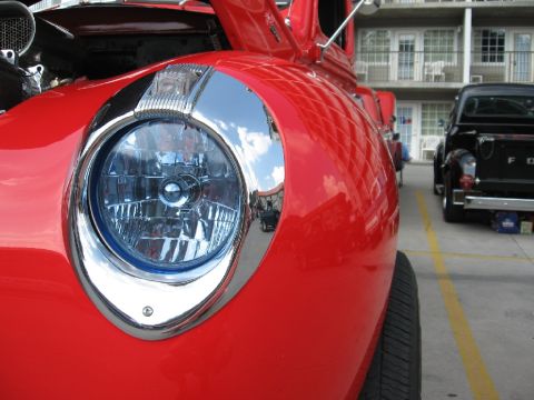 1966 Ford F-100 - Front view of a red truck's fender and headlight, with another truck in the background.