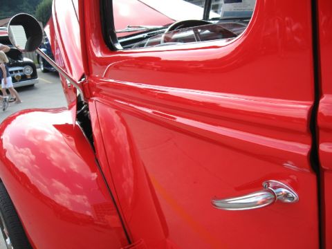 1966 Ford F-100 - A bright red vintage truck is shown from the side, with a glimpse of its interior and another vehicle in the background.