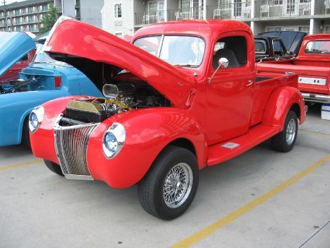 1966 Ford F-100 - A red pickup truck is parked next to a blue vehicle, with another truck behind it.