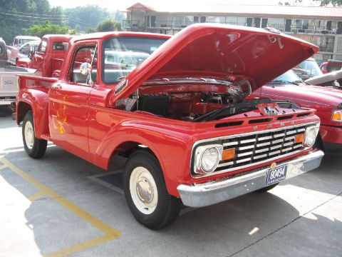1966 Ford F-100 - A red pickup truck is parked with its hood open, revealing the engine. Another truck is visible behind it.