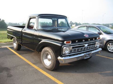 1966 Ford F-100 - This black 1966 Ford F-100 pickup truck is parked next to another vehicle.