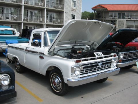 1966 Ford F-100 - A white pickup truck is parked with its hood open, revealing the engine compartment. Other vehicles are visible nearby.