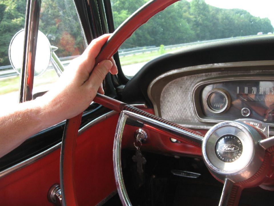 Red steering wheel and dashboard of a 1966 Ford F-100, with a hand on the wheel