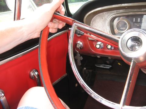 1966 Ford F-100 - The interior of a 1966 Ford F-100, a red dashboard and steering wheel, with a hand resting on the wheel.