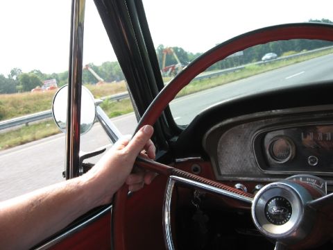1966 Ford F-100 - View from inside a classic Ford truck, showing the steering wheel, dashboard, and a glimpse of the road ahead.