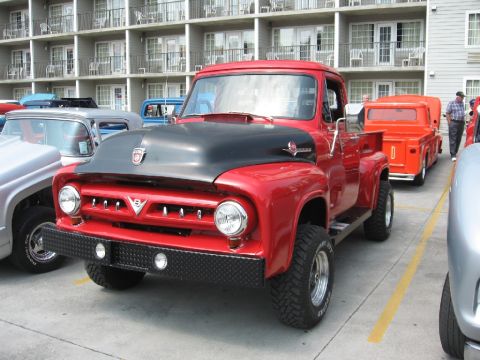 1966 Ford F-100 - A red pickup truck with a black hood and diamond plate bumper is parked next to other vehicles.