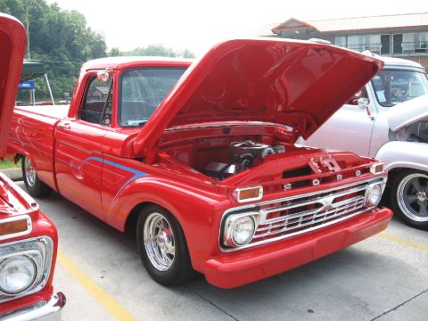 1966 Ford F-100 - Red 1966 Ford F-100 pickup truck with custom flames and hood open at a car show.