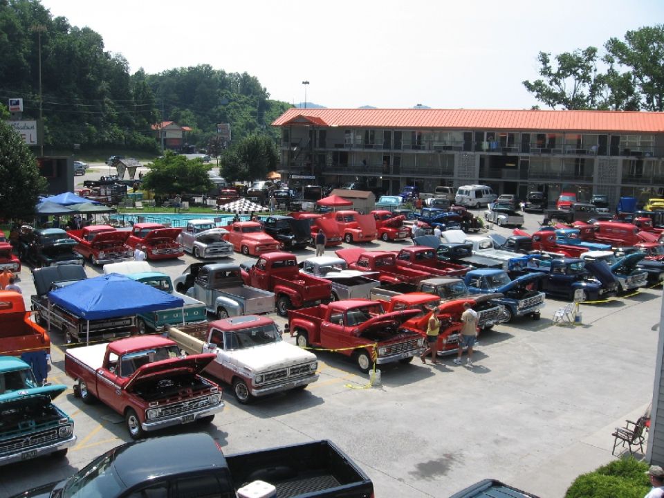 Many Ford F-100 trucks from the 1960s parked in a lot outside a motel