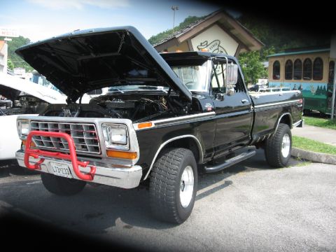 1966 Ford F-100 - A black pickup truck with its hood open is parked outside a building with a trolley in the background.