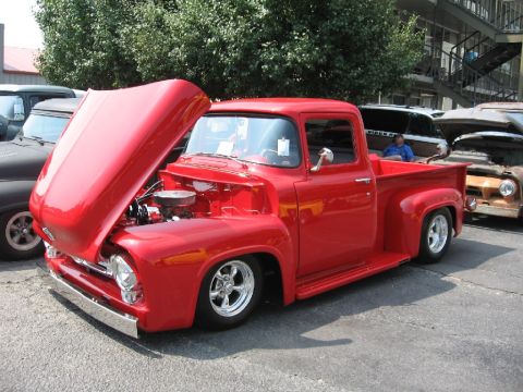 1966 Ford F-100 - A bright red 1955 Ford F-100 pickup truck is parked with its hood open, showing the engine bay.