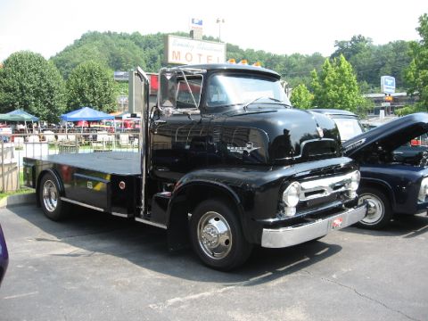 1966 Ford F-100 - Black flatbed truck parked next to another truck with its hood open at an outdoor event.