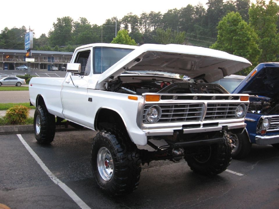 White Ford F-Series pickup truck with hood open, lifted suspension, and large tires