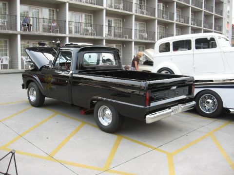 1966 Ford F-100 - A black 1966 Ford F-100 pickup truck is parked next to another vehicle with its hood open.