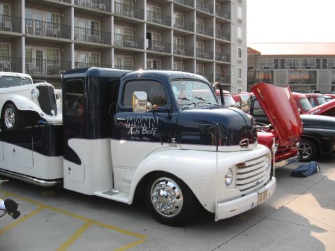 1966 Ford F-100 - Ford COE tow truck with a hot rod on its trailer, parked in front of a hotel with other classic trucks.