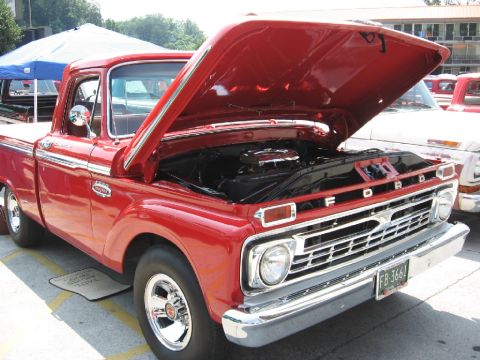 1966 Ford F-100 - A red 1965 Ford F-100 truck is displayed with its hood open, revealing the engine bay.