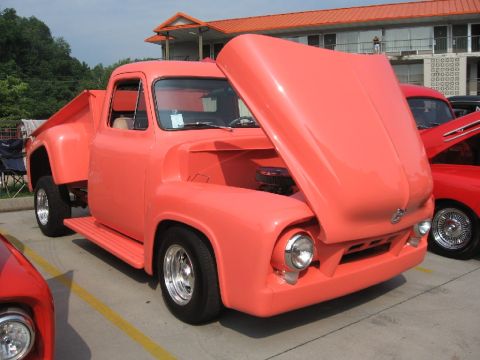 1966 Ford F-100 - A coral-colored 1950s Ford F-Series truck is displayed with its hood up, parked alongside another vehicle.