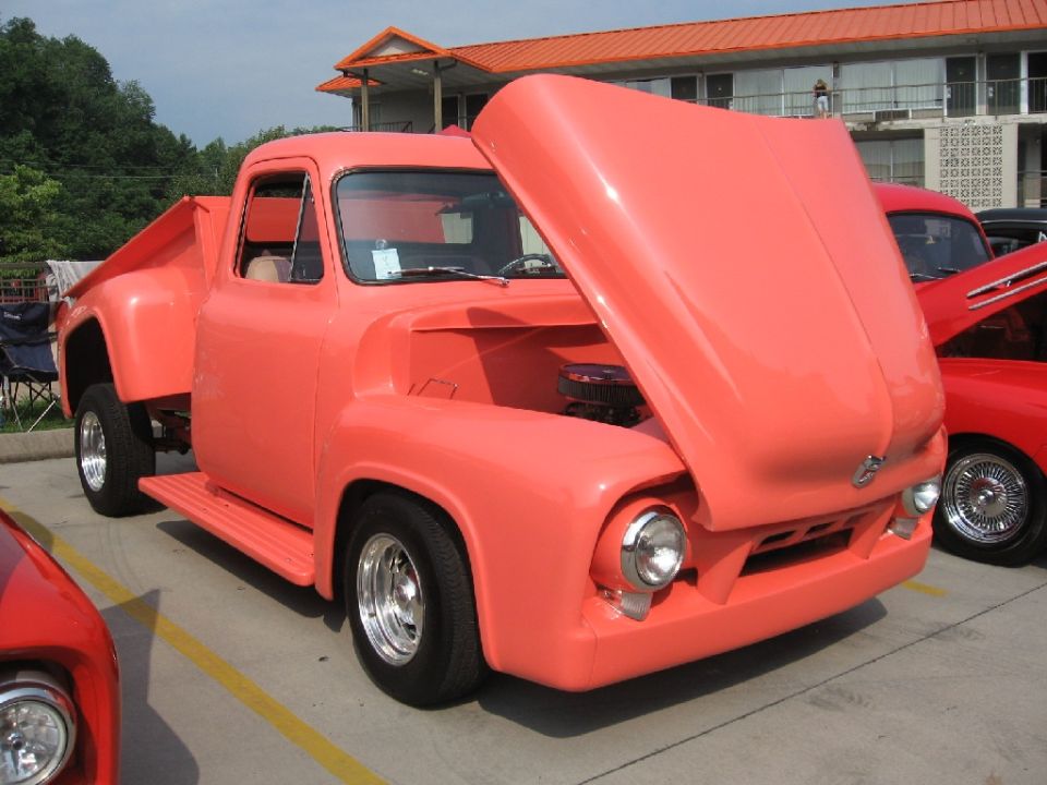 Coral 1950s Ford F-Series truck with hood open, parked next to a red car