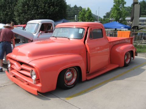 1966 Ford F-100 - A coral 1955 Ford F-series truck is parked next to another truck at an outdoor event.