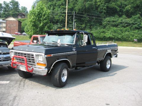 1966 Ford F-100 - This black Ford F-150 pickup truck features a red brush guard and chrome wheels, parked outdoors with other vehicles nearby.