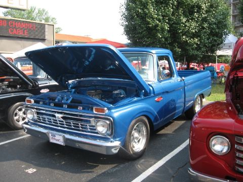 1966 Ford F-100 - A blue pickup truck is parked with its hood open, showing the engine. Another vehicle is partially visible to the right.