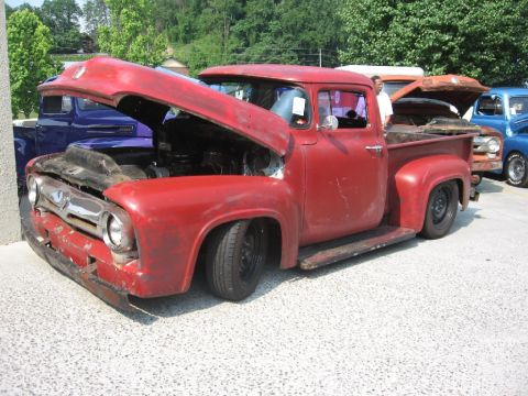 1966 Ford F-100 - A red 1956 Ford F-100 pickup truck is displayed with its hood open, revealing the engine and a lowered suspension.